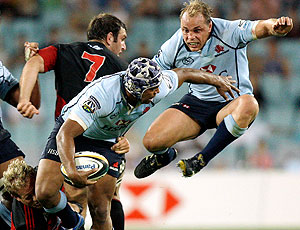 Crusaders' Andy Ellisleft, bottom left, tackles the Waratahs' Dean Mumm as his captain Phil Waugh jumps to make room for a pass during their Super 14 rugby union game at the Olympic Stadium in Sydney, Australia, Saturday, March 21, 2009. (AP Photo/Rick Rycroft)