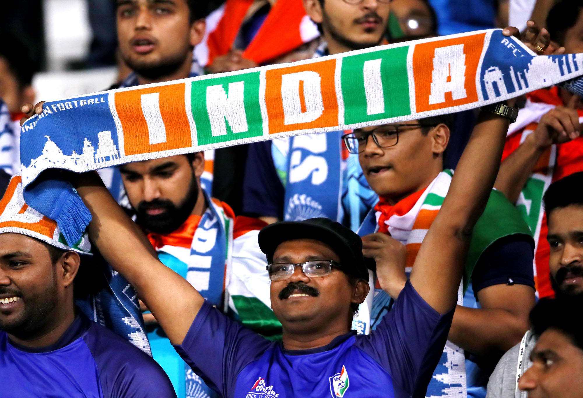 An Indian football fan holds aloft a scarf with the word 'INDIA' printed on it.