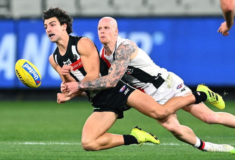 Josh Daicos of the Magpies handballs whilst being tackled