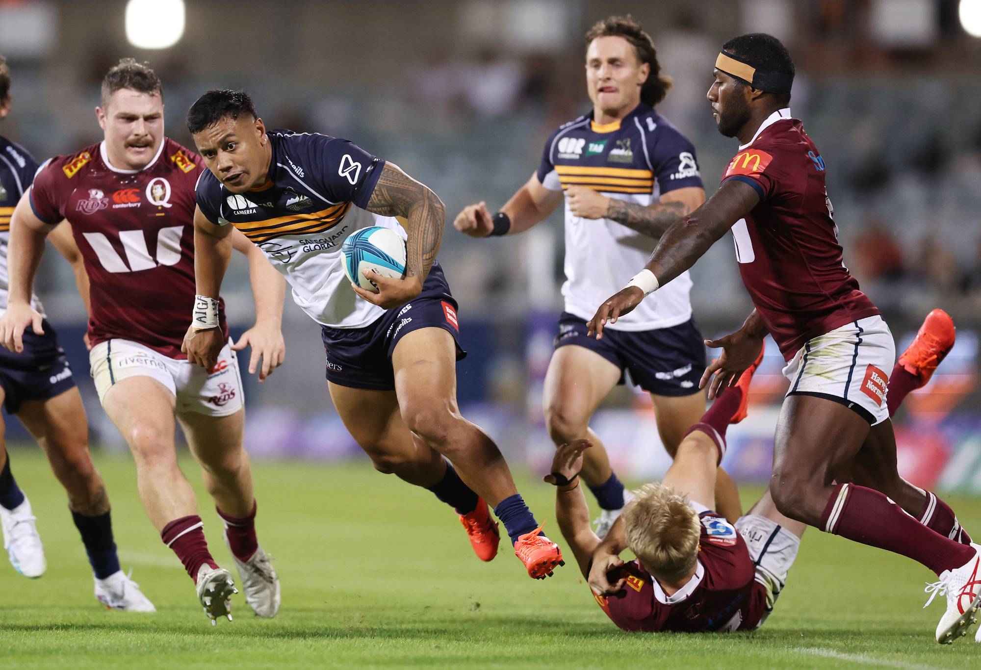 Len Ikitau of the Brumbies breaks through the tackle of Tom Lynagh of the Reds