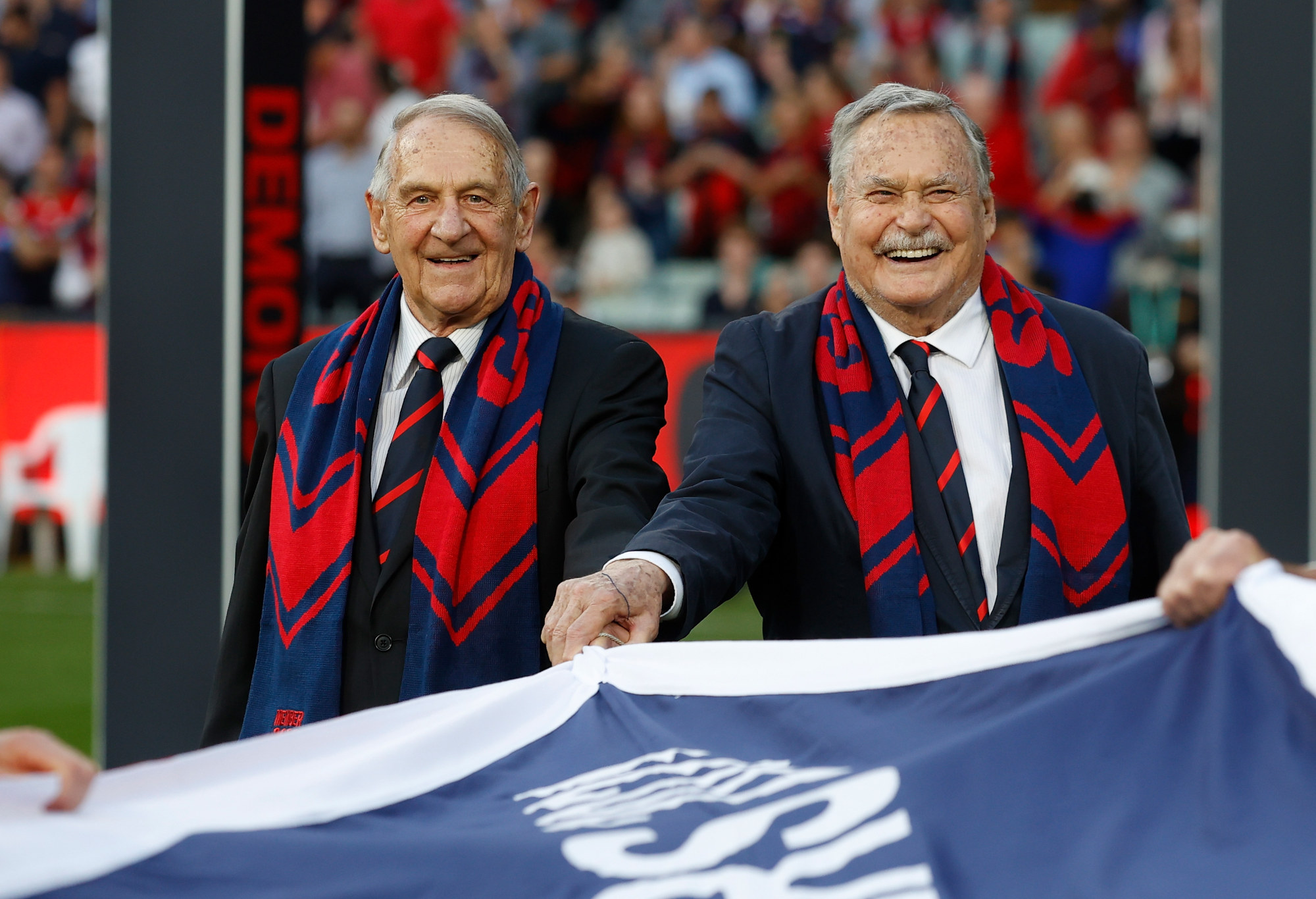 Hassa Mann (L) and Ron Barassi carry Melbourne's 2021 premiership flag.