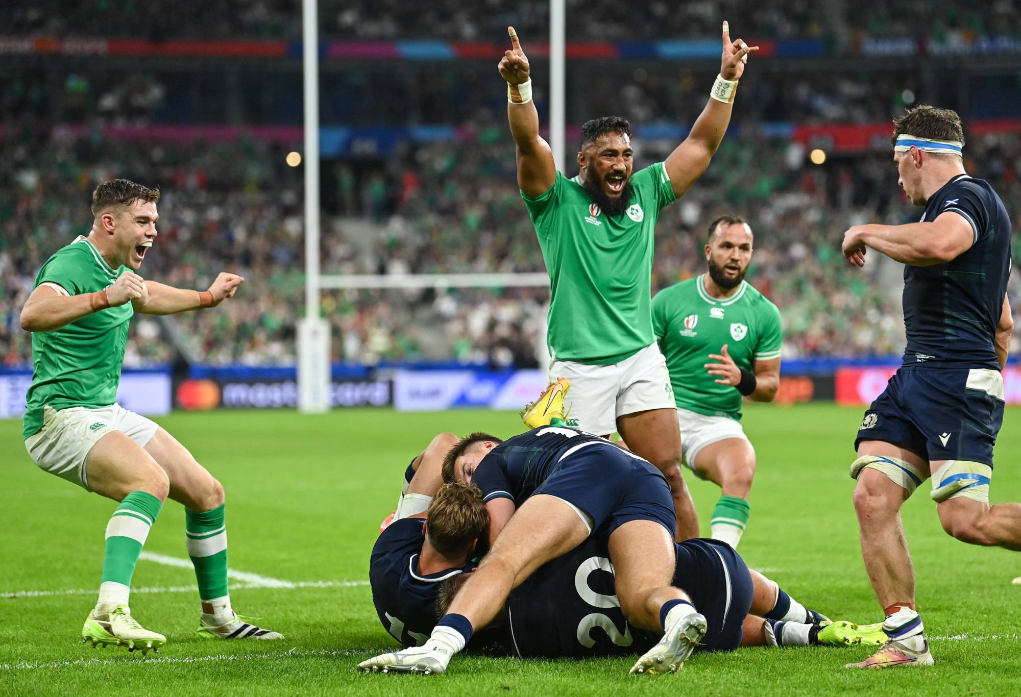 Hugo Keenan of Ireland, hidden, scores his side's fourth try, despite the efforts of Scotland's Duhan van der Merwe, left, and Matt Fagerson, as teammates Garry Ringrose, left, and Bundee Aki celebrate, during the 2023 Rugby World Cup Pool B match between Ireland and Scotland at the Stade de France in Paris, France. (Photo By Ramsey Cardy/Sportsfile via Getty Images)
